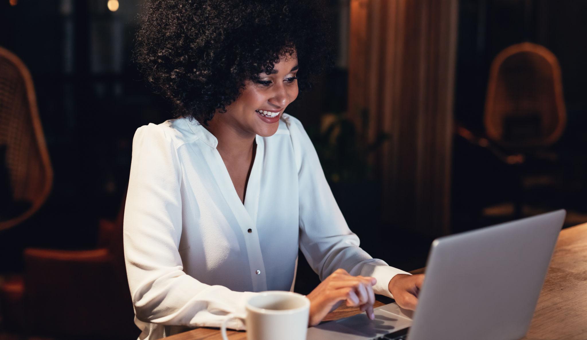 Woman smiling while working on a laptop at a cafe table